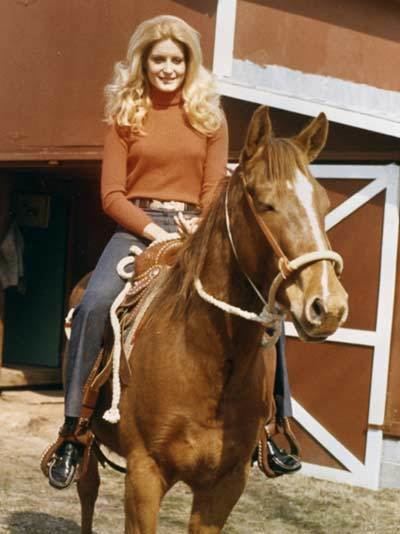 Wilma Smith riding a horse wearing an orange sleeves, gray pants and black shoes