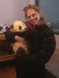 Windland Smith Rice smiling and carrying a baby panda while wearing a read and black coat