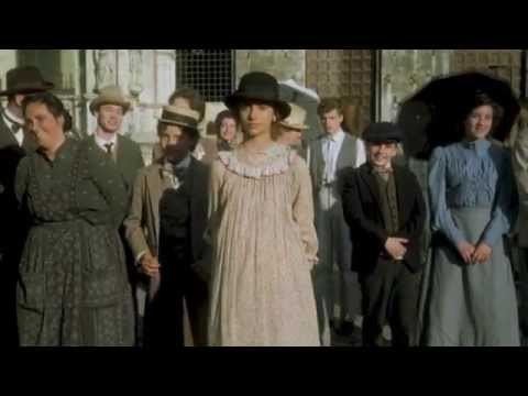 Debora Caprioglio standing in the crowd while wearing a black hat and beige dress in a movie scene from the 1994 film, With Closed Eyes