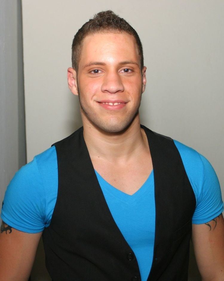 Wolf Hudson smiling while wearing a blue shirt and black vest
