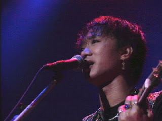 Wong Ka Kui with a sad face while singing and playing guitar with a microphone in front of him.