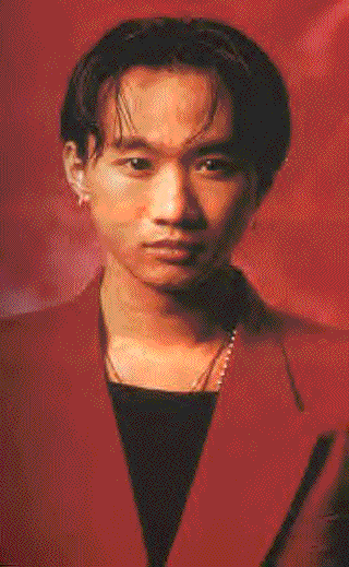 Wong Ka Kui with a serious face, wearing a necklace, and a red coat over a black shirt.