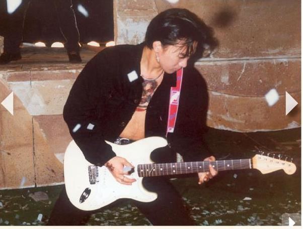 Wong Ka Kui passionately plays guitar, wearing a black jacket and black pants.