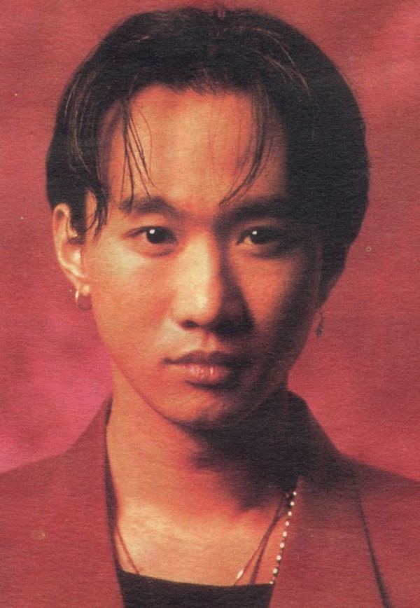 Wong Ka Kui with a serious face, wearing a necklace, and a red coat over a black shirt.