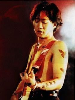 Wong Ka Kui with a serious face while playing guitar, topless, and wearing black pants.