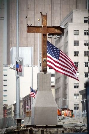 The World Trade Center cross and behind of it is the three Flags of the United States of America