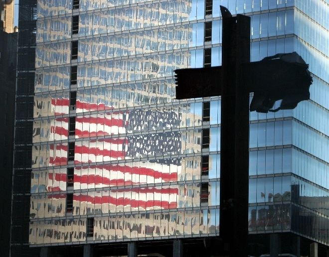 The World Trade Center cross and behind of it is the reflection of the Flag of the United States of America in the building