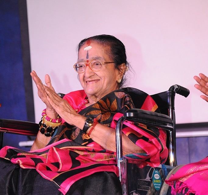 Y. G. Parthasarathy in her wheelchair wearing black and pink dress while clapping