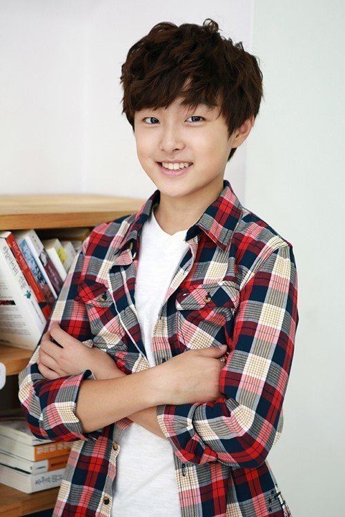 Yoon Chan-young smiling in crossed arms is a South Korean actor with a bookshelf in the background, in a brown messy hairstyle, wearing a white V-neck shirt and a checkered long sleeve.