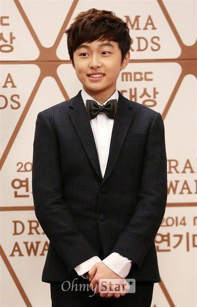 Yoon Chan-young smiling and holding his hands, a South Korean actor attending the 2014 MBC Drama Awards at MBC in December 2014, in Seoul, South Korea, with a brown messy hairstyle wearing a bowtie on a white collared long sleeve and a black coat.