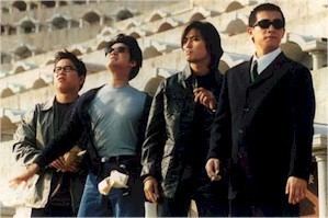 The cast of the 1996 film Young and Dangerous 2 starring- Ekin Cheng has black hair, serious, and wears a black top under a black jacket and pants. Jordan Chan has black hair, is serious, and wears a gray shirt under a black jacket and denim pants with a small bag on his left. Gigi Lai is serious, has black hair, left hand up, and wears a black top under a black jacket and pants. Anthony Wong Chau-sang is serious, has black hair, wears black eyeglasses, white long sleeves under a black suit and pants.