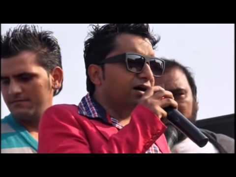 Yudhvir Manak holding a microphone while wearing shades, red coat and checkered long sleeves