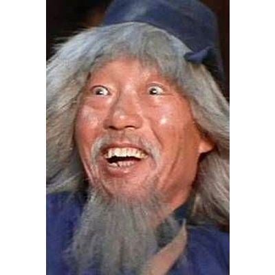 Yuen Siu-tien with a funny face, with white hair, a white beard, and wearing a blue hat and a blue shirt.