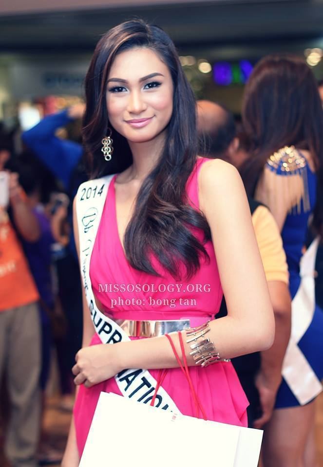 Yvethe Marie Santiago with a tight-lipped smile while carrying a white paper bag, with a black wavy hair, and wearing a pink sleeveless dress with a silver belt, earrings, bracelet, and the sash of 2014 Binibining Pilipinas Supranational