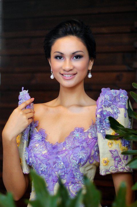 Yvethe Marie Santiago smiling and holding the sleeve of her gown while wearing pearl earrings and a light-green filipiniana gown with purple and yellow flower design