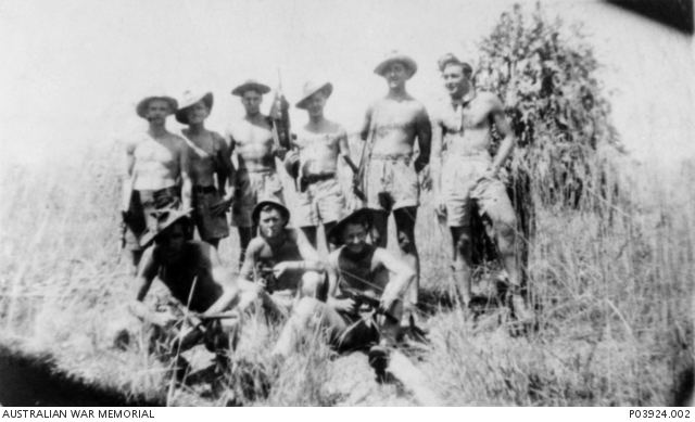 Members of the Z Special Unit smiling together in a forest background, with some of them having guns in their hands, they are wearing hats, topless and short pants