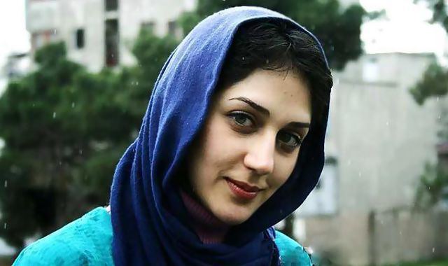 Zahra Amir Ebrahimi smiling with her black hair and trees in the background, wearing a blue hijab and a light greenish-blue blouse