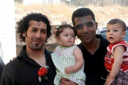 Free Nabil Al-Raee and Zakaria Zubeidi smiling while carrying a toddler
