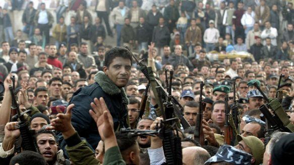 Zakaria Zubeidi is surrounded by people with guns while he is wearing a gray and blue fur jacket