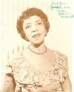 Portrait of Zara Cully smiling with short curly hair while wearing blouse and necklace