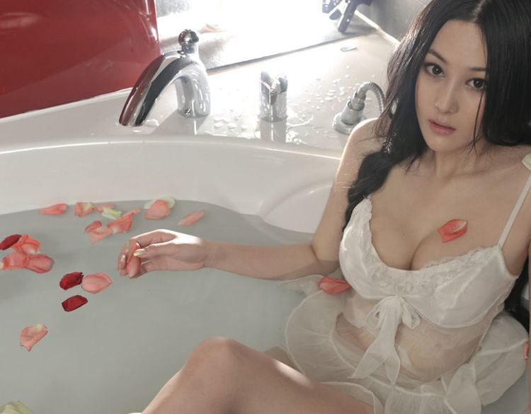 Zhang Xinyu sitting in a bathtub with flowers and wearing a white, sleeveless lace dress.