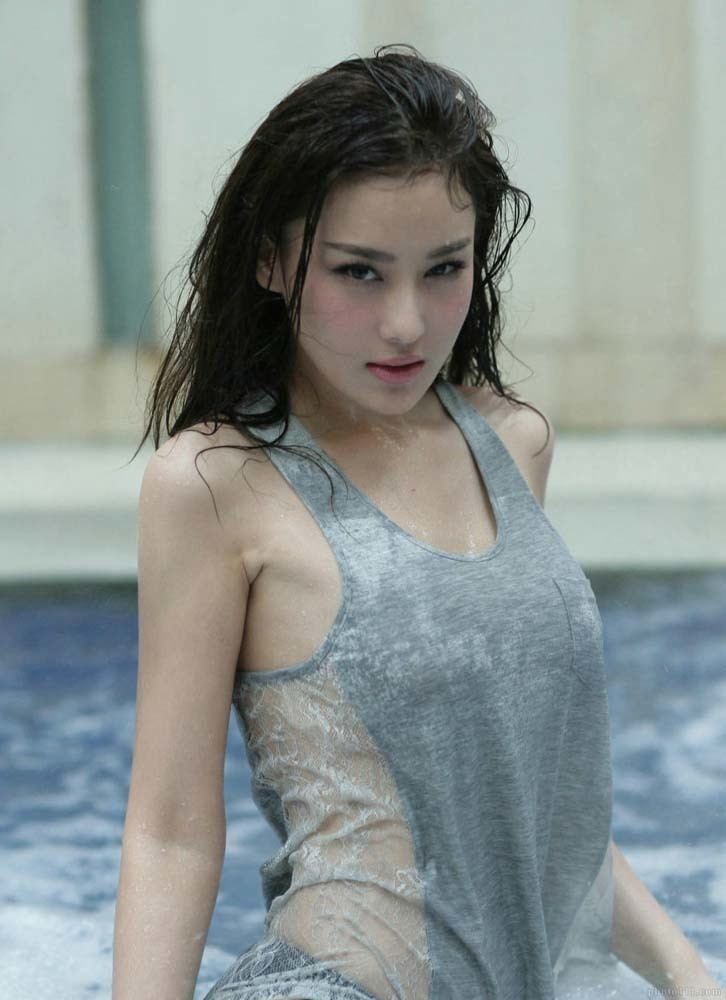 Zhang Xinyu posing seductively in a pool with her hair wet while wearing a gray, see through shirt.