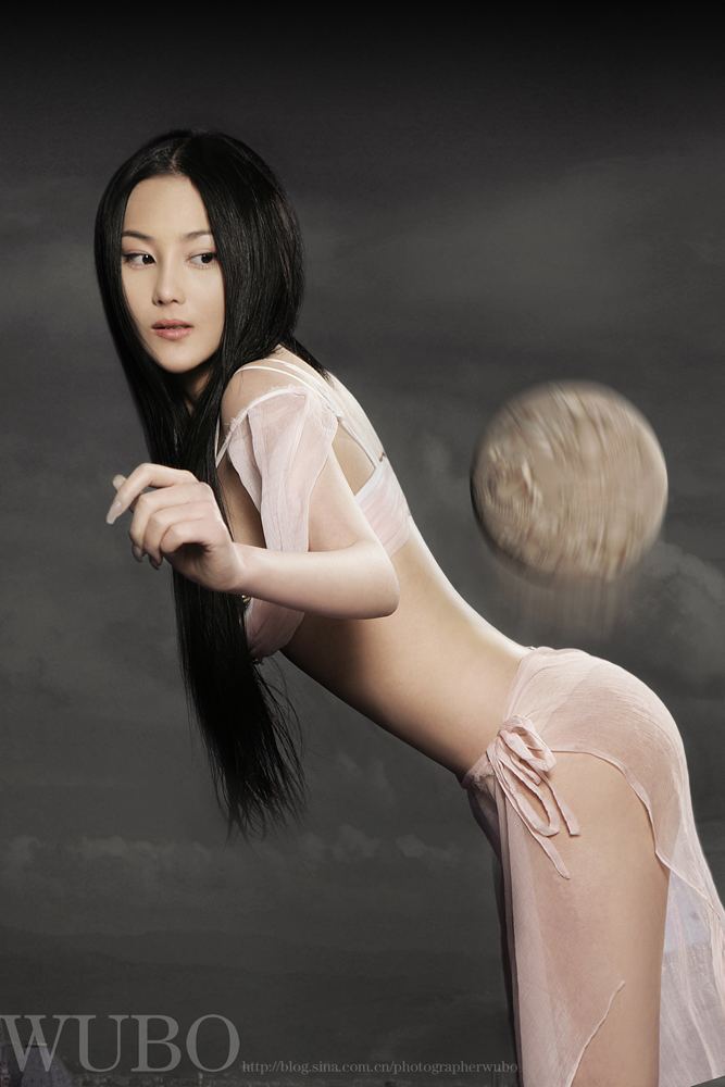 Zhang Xinyu playing with a ball in a beach and wearing a cream colored silk bikini.