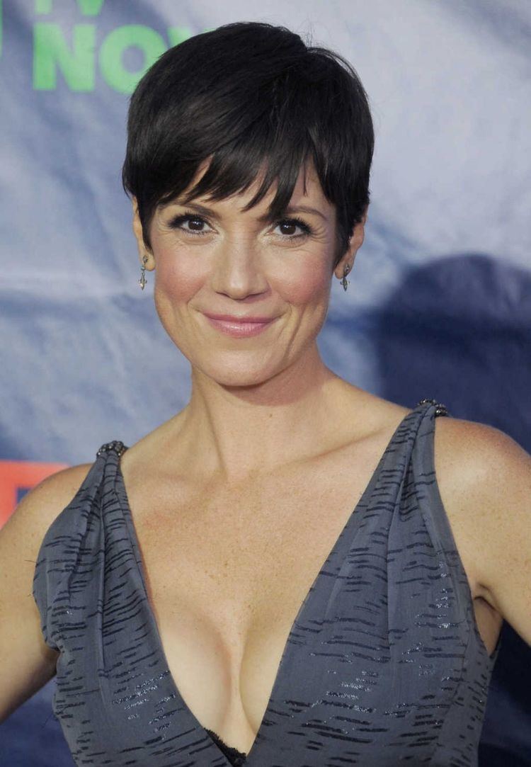 Zoe McLellan's tight lipped smile while wearing gray dress and earrings