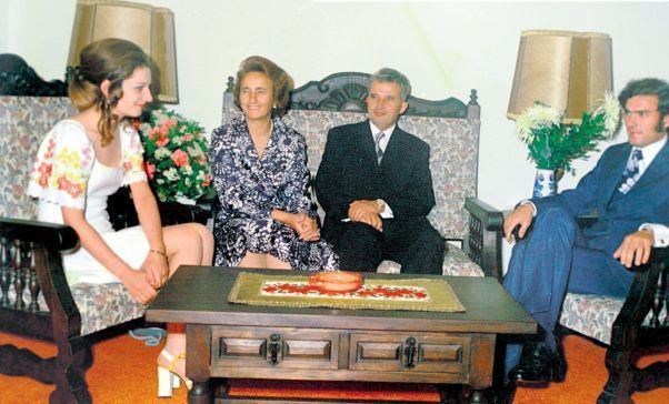 Zoia Ceaușescu sitting down with a group of people and wearing a white dress with floral design.