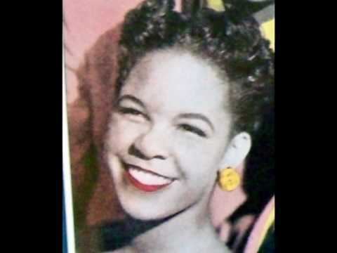 Zola Taylor with a smiling face and wearing yellow earrings.