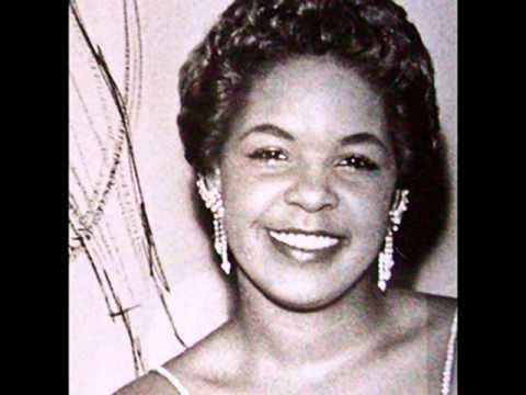 Zola Taylor smiling, with curly hair and wearing earrings.