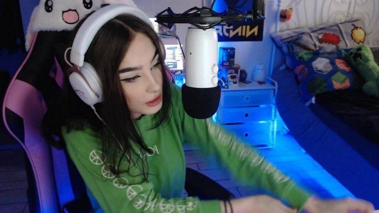 Zookdook speaking while sitting on a black and pink gaming chair and she is wearing a white headphone and a green long sleeve blouse