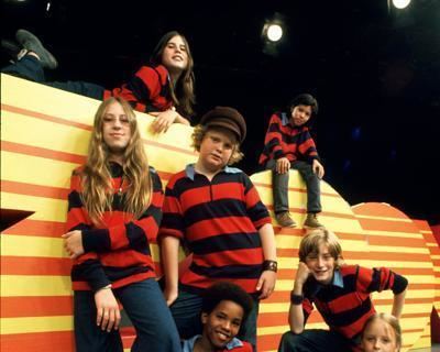 Maura Mullaney, Kenny Pires, Donna Moore, Mike Dean, Joe Shrand, Leon Mobley, and Edith Mooers (from upper left to lower right) are wearing red and black striped long sleeve shirts, casts of Zoom, an American live-action children's television series.